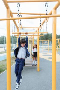 A boy in a school uniform enjoys playing on monkey bars outdoors.