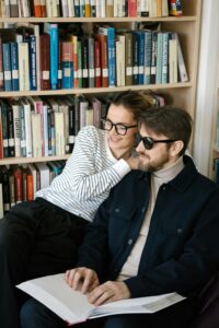 A man and woman sitting in a library reading a braille book together, smiling.