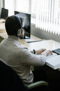 A visually impaired man reading a braille book indoors with headphones on.