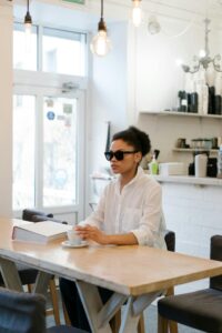 A visually impaired woman reads a Braille book at a cozy cafe, embracing education and independence.