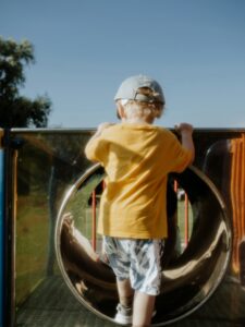 A young child climbing a playground slide on a sunny summer day, enjoying outdoor play.
