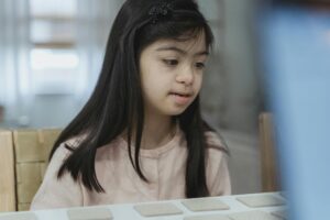 A young girl with Down syndrome playing attentively at a desk indoors. Bright and warm ambiance.