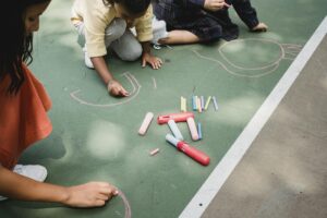 Kids engaged in creative outdoor activity drawing with colorful chalk on pavement.