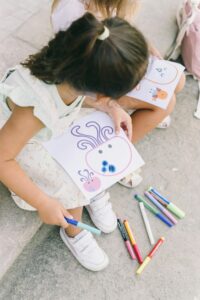 Two young girls drawing with colorful markers on paper, showcasing creativity and friendship.