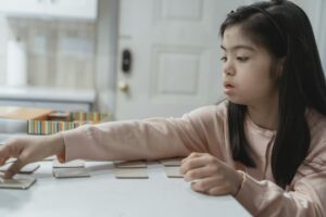 Young Asian girl with Down Syndrome engaged in a game indoors, wearing a pink sweater.