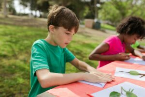 Young kids engage in outdoor crafting activities during summer camp, learning and having fun.